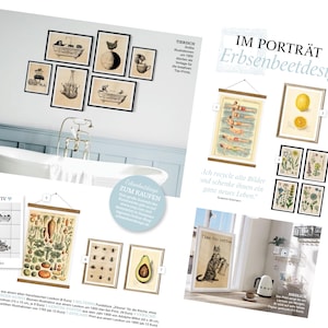 May include: A collection of vintage botanical prints in black frames, featuring illustrations of lemons, flowers, and a cat. The prints are displayed on a white wall with a white bathtub in the background. The text "IM PORTR&Auml;T Erbsenbeetdesign" is visible in the top right corner of the image.