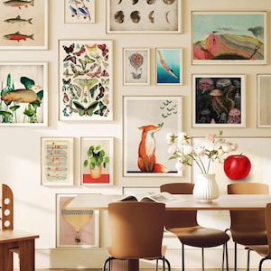 May include: A dining room with a white wall featuring a gallery wall of framed prints. The prints include images of fish, butterflies, a fox, a jellyfish, and a red apple. There is a wooden chair and a table with four chairs.