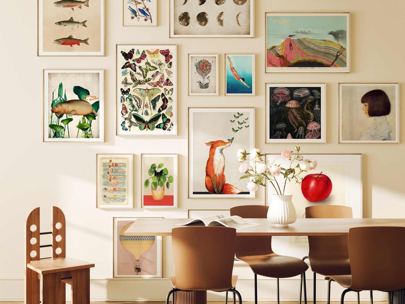 May include: A dining room with a white wall featuring a gallery wall of framed prints. The prints include images of fish, butterflies, a fox, a jellyfish, and a red apple. There is a wooden chair and a table with four chairs.