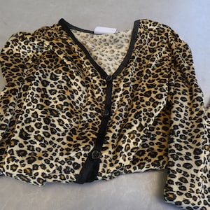 Può includere: Un cardigan con stampa leopardata con chiusura a bottoni neri e maniche lunghe. Il cardigan è realizzato in un tessuto morbido e setoso.
