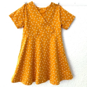 May include: A mustard yellow dress with a white anchor print and a wrap style neckline. The dress has short sleeves and a flared skirt.