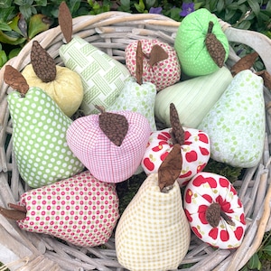May include: A wicker basket filled with handmade fabric pears and apples. The pears are in various patterns, including polka dots, gingham, and floral prints. The apples are red and white with a red apple design.