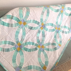 Könnte beinhalten: Eine weiße Steppdecke mit einem Doppelringmuster in Blautönen und Grün. Die Steppdecke ist aus verschiedenen Stoffen gefertigt und hat ein gestepptes Design.