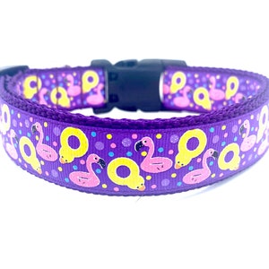 May include: A purple dog collar with a black plastic buckle. The collar features a repeating pattern of pink flamingos and yellow pool floats. Small, colorful polka dots are scattered across the collar's surface.