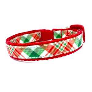 May include: A red and plaid dog collar with a plastic buckle. The collar features a pattern of red, green, and white squares. The collar is designed for a small dog or puppy.