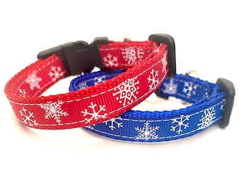 May include: Two dog collars, one red and one blue, are displayed. Both collars feature a white snowflake pattern. The collars have black plastic buckles. The collars are designed for pets.