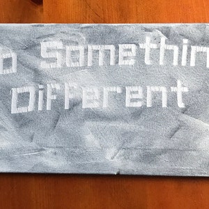 May include: A grey canvas sign with the text "Do Something Different" written in white block letters.