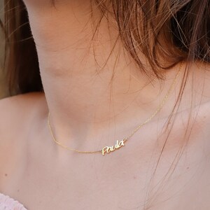 May include: A gold chain necklace with the name 'Paula' written in cursive on a pendant.