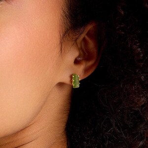 May include: A close-up of a person's face with a green and gold earring in their left ear.