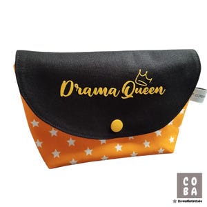Könnte beinhalten: Schwarze und orangefarbene Reißverschlusstasche mit weißem Sternenmuster. Die Tasche hat einen gelben Knopf und steht in gelben Buchstaben mit einer Krone über dem Text "Drama Queen".