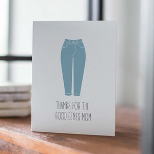 White card with illustration of mom jeans with "thanks for the good genes mom" written below. Lifestyle photo of card on shelf.