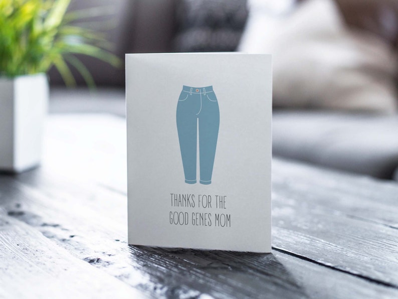 White card with illustration of mom jeans with "thanks for the good genes mom" written below. Lifestyle photo of card on table.