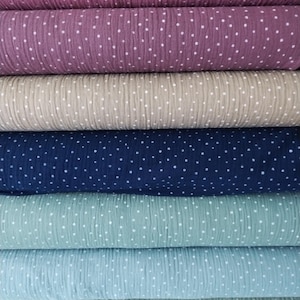 Könnte beinhalten: Ein Stapel von sechs Stoffrollen mit weißen Punkten auf verschiedenen Farben, darunter Rosa, Beige, Dunkelblau, Hellblau und Grün.