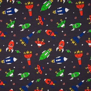 May include: A dark blue fabric with a repeating pattern of colorful rockets, spaceships, and planets. The rockets are red, green, and blue with yellow flames. The spaceships are blue with white windows. The planets are orange, yellow, and green.