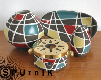 Op de afbeelding: Een verzameling keramische stukken in mid-century modern stijl. De set bevat een ronde vaas, een ovale schaal, een kleine vaas en een warmer met messing rand. Elk stuk is bruin met een geometrisch patroon van rood, geel, turquoise en wit.