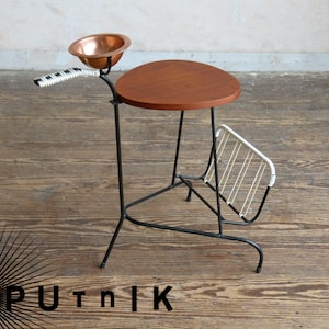May include: A mid-century modern side table with a round wooden top, a metal frame, and a magazine rack. The table has a copper bowl attached to the side.