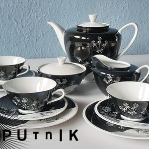 May include: A black and white tea set with a teapot, sugar bowl, creamer, cups, and saucers. The set features a floral design and is set against a light blue background. The cups and saucers are white inside.