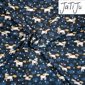 Könnte beinhalten: Ein dunkelblauer Stoff mit einem sich wiederholenden Muster aus weißen Einhörnern mit Regenbogenmähne und -schwanz. Die Einhörner galoppieren vor einem Hintergrund aus weißen Sternen und grauen Wolken. Der Stoff hat den Text "JaTiJu" in weiß in der oberen rechten Ecke gedruckt.