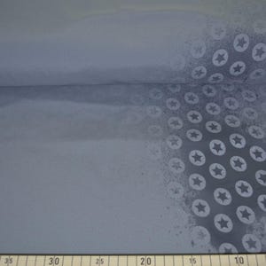 Könnte beinhalten: Eine Rolle hellblauen Stoffes mit einem sich wiederholenden Muster aus weißen Sternen in Kreisen. Der Stoff ist gefaltet und zeigt eine strukturierte Oberfläche. Das Sternmuster ist auf der rechten Seite dichter.