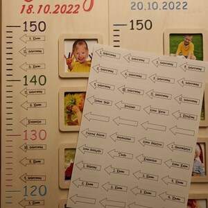 Pode incluir: Um gr&aacute;fico de crescimento de madeira com uma r&eacute;gua marcada em cent&iacute;metros, com os nomes Emily e Timo com suas datas de nascimento, 18.10.2022 e 20.10.2022, respectivamente. O gr&aacute;fico inclui espa&ccedil;os para fotos e adesivos para marcar marcos.