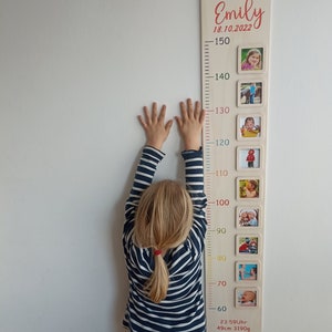 Pode incluir: Um gr&aacute;fico de crescimento de madeira com fundo branco e n&uacute;meros coloridos. O gr&aacute;fico tem uma moldura com uma foto de uma crian&ccedil;a em diferentes idades. O gr&aacute;fico est&aacute; etiquetado como "Emily 18.10.2022" e inclui a altura e o peso da crian&ccedil;a ao nascer.