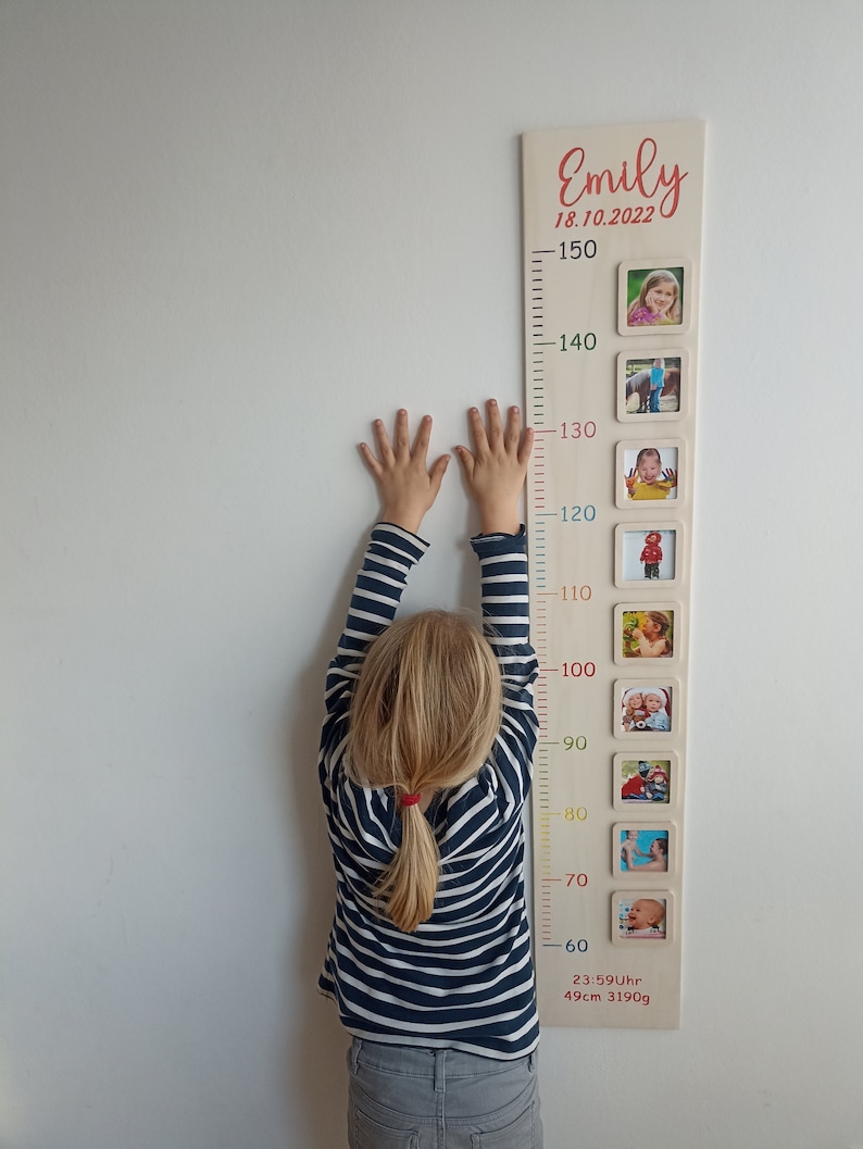 Pode incluir: Um gr&aacute;fico de crescimento de madeira com fundo branco e n&uacute;meros coloridos. O gr&aacute;fico tem uma moldura com uma foto de uma crian&ccedil;a em diferentes idades. O gr&aacute;fico est&aacute; etiquetado como "Emily 18.10.2022" e inclui a altura e o peso da crian&ccedil;a ao nascer.