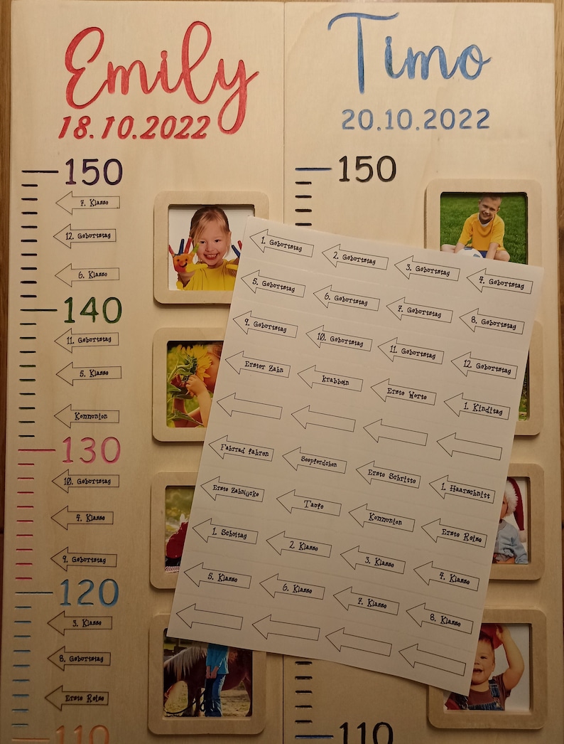 Op de afbeelding: Een witte houten groeimeter met twee secties, een voor Emily en een voor Timo. Elke sectie heeft een liniaal met markeringen voor de hoogte in centimeters. De kaart bevat ook een fotolijst met een foto van een kind en een set stickers met pijlen en tekst die mijlpalen aangeven zoals verjaardagen en schooljaren.