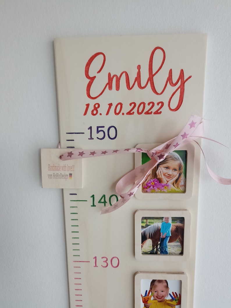 Pode incluir: Um gr&aacute;fico de crescimento de madeira com uma fita rosa e estrelas, incluindo um nome, uma data e tr&ecirc;s molduras para fotos. O gr&aacute;fico tem um fundo branco com marcas verdes e rosas. O texto no gr&aacute;fico diz "Emily 18.10.2022".