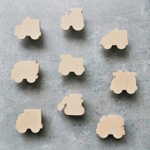 Può includere: Nove forme di legno ritagliate di diversi veicoli, tra cui un trattore, un camion, una betoniera, un camion dei pompieri, un'auto della polizia e un veicolo da costruzione. Le forme sono tutte in legno marrone chiaro e sono disposte in una griglia su uno sfondo grigio.