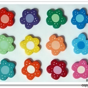 Könnte beinhalten: Zwölf bunte, holzartige Knöpfe in Blumenform mit weißen Punkten. Jeder Knopf hat eine andere Farbe und einen weißen Mittelkreis.