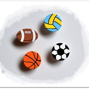 Peut inclure: Quatre ornements en bois en forme de ballon de sport. Un ballon de football brun et blanc, un ballon de volley-ball bleu et jaune, un ballon de football noir et blanc et un ballon de basket-ball orange.