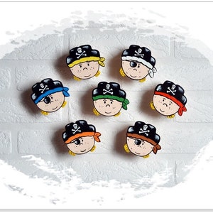 May include: Seven wooden pirate head ornaments with black hats, eyepatches, and different colored bandanas. The bandanas are yellow, white, blue, green, orange, brown, and red.
