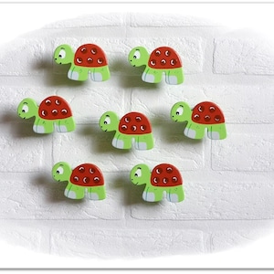 May include: Eight wooden turtle figurines with green shells and red spots. The turtles have white feet and black eyes.