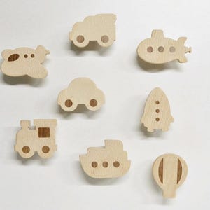 May include: Wooden wall hooks shaped like various vehicles, including a plane, car, train, submarine, rocket, boat, and hot air balloon. The hooks are all made of natural wood and have a light brown color.