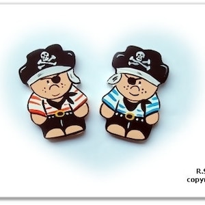 May include: Two wooden figurines of pirates wearing black hats with skull and crossbones, one with a red and white striped shirt and the other with a blue and white striped shirt.