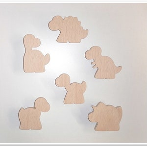 Può includere: Sei forme di dinosauro in legno in varie pose, tutte tagliate dallo stesso legno marrone chiaro.