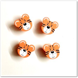 Könnte beinhalten: Vier orangefarbene Holztigerkopf-Ornamente mit schwarzen Streifen und weißen Gesichtern.