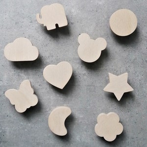 Peut inclure: Neuf crochets muraux en bois de différentes formes, notamment un nuage, un cœur, une étoile, un papillon, un éléphant, une lune, une fleur et un cercle avec deux oreilles. Les crochets sont tous en bois naturel et ont une couleur brun clair.