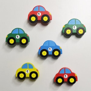 Op de afbeelding: Zes houten speelgoedauto's in verschillende kleuren, elk met het nummer "1" aan de zijkant. De auto's zijn rood, groen, blauw, geel en twee rode auto's.