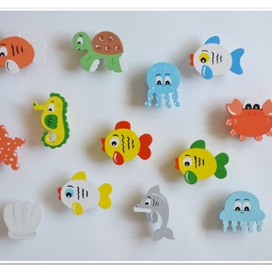 May include: A set of 11 wooden sea creature toys, including a starfish, seahorse, turtle, crab, two jellyfish, and five fish. The toys are painted in bright colors, including red, orange, yellow, green, blue, and gray.