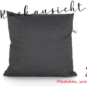 May include: A dark gray pillow with the German word "R&uuml;ckansicht" written in black above it. The text "M&auml;dchen sucht Kleid" is written in red below the pillow.