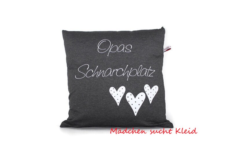 May include: A gray pillow with white text that says "Opa's Schnarchplatz" and three white hearts with black polka dots. The text "Madchen sucht Kleid" is printed in red at the bottom of the pillow.
