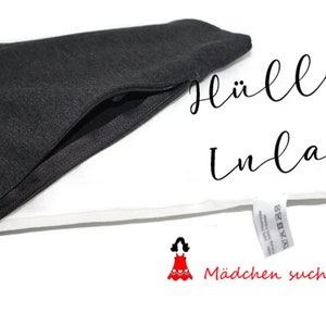 May include: A black zippered pouch with a white fabric inlay. The pouch is open and the inlay is visible. The text "H&uuml;lle + Inlay" is written in black cursive on the white fabric. The text "M&auml;dchen sucht Kleid" is written in red below the inlay.