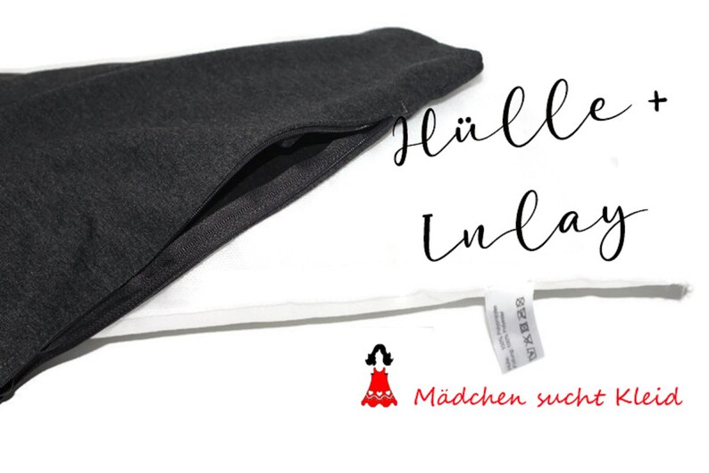 May include: A black zippered pouch with a white fabric inlay. The pouch is open and the inlay is visible. The text "H&uuml;lle + Inlay" is written in black cursive on the white fabric. The text "M&auml;dchen sucht Kleid" is written in red below the inlay.