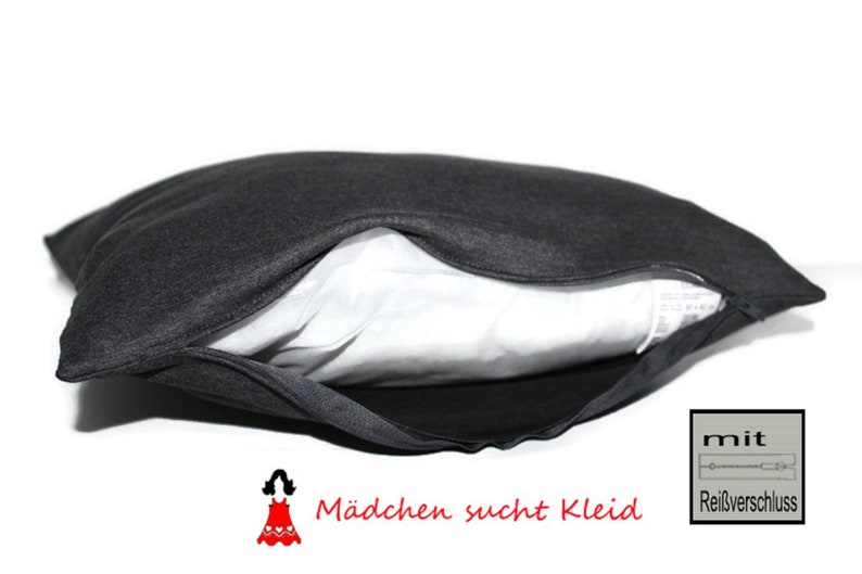 May include: A black pillow with a zipper opening, showing a white inner lining. The pillow has the text "M&auml;dchen sucht Kleid" and "mit Rei&szlig;verschluss" printed on it.