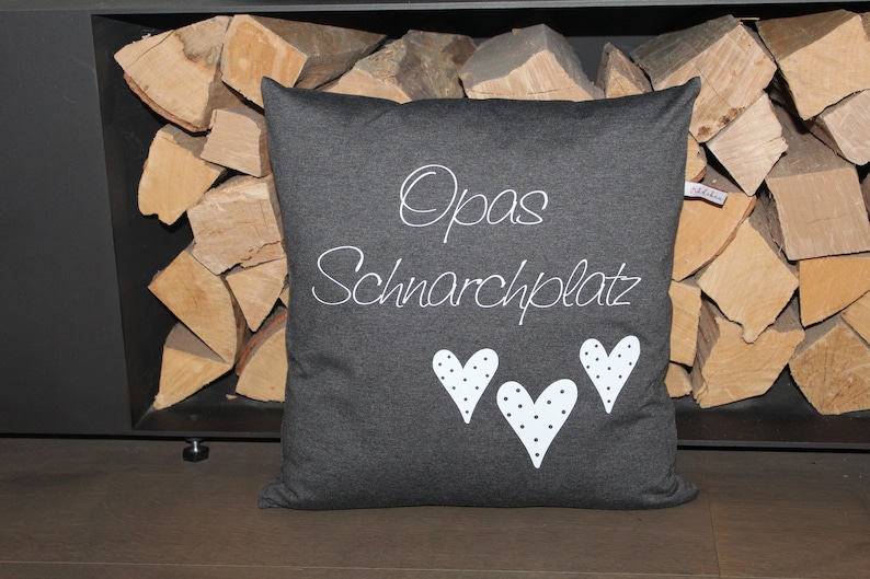May include: A gray pillow with white text that says "Opa's Schnarchplatz" and three white hearts with black polka dots.