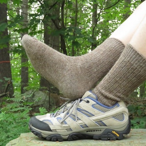 May include: A pair of brown wool hiking socks with a pair of gray hiking boots. The boots have a black Vibram sole and a blue and gray mesh panel.