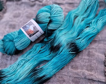 May include: A skein of teal and black hand-dyed yarn with a label that reads "Luminous" and "mini skein".