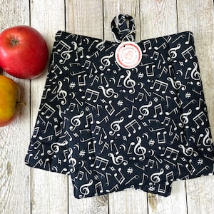 Könnte beinhalten: Zwei schwarze Topflappen mit einem weißen Notenmuster. Die Topflappen sind in der Mitte gefaltet und haben ein weißes Etikett mit einem roten Herzen.