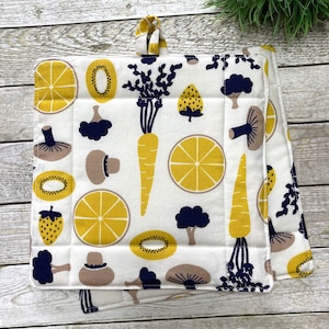 Könnte beinhalten: Zwei weiße Baumwoll-Topflappen mit gestepptem Design. Die Topflappen haben ein sich wiederholendes Muster aus gelben Zitronen, Karotten, Kiwis, Erdbeeren, Pilzen und Brokkoli. Die Topflappen haben einen dunkelblauen Saum und eine Schlaufe zum Aufhängen.